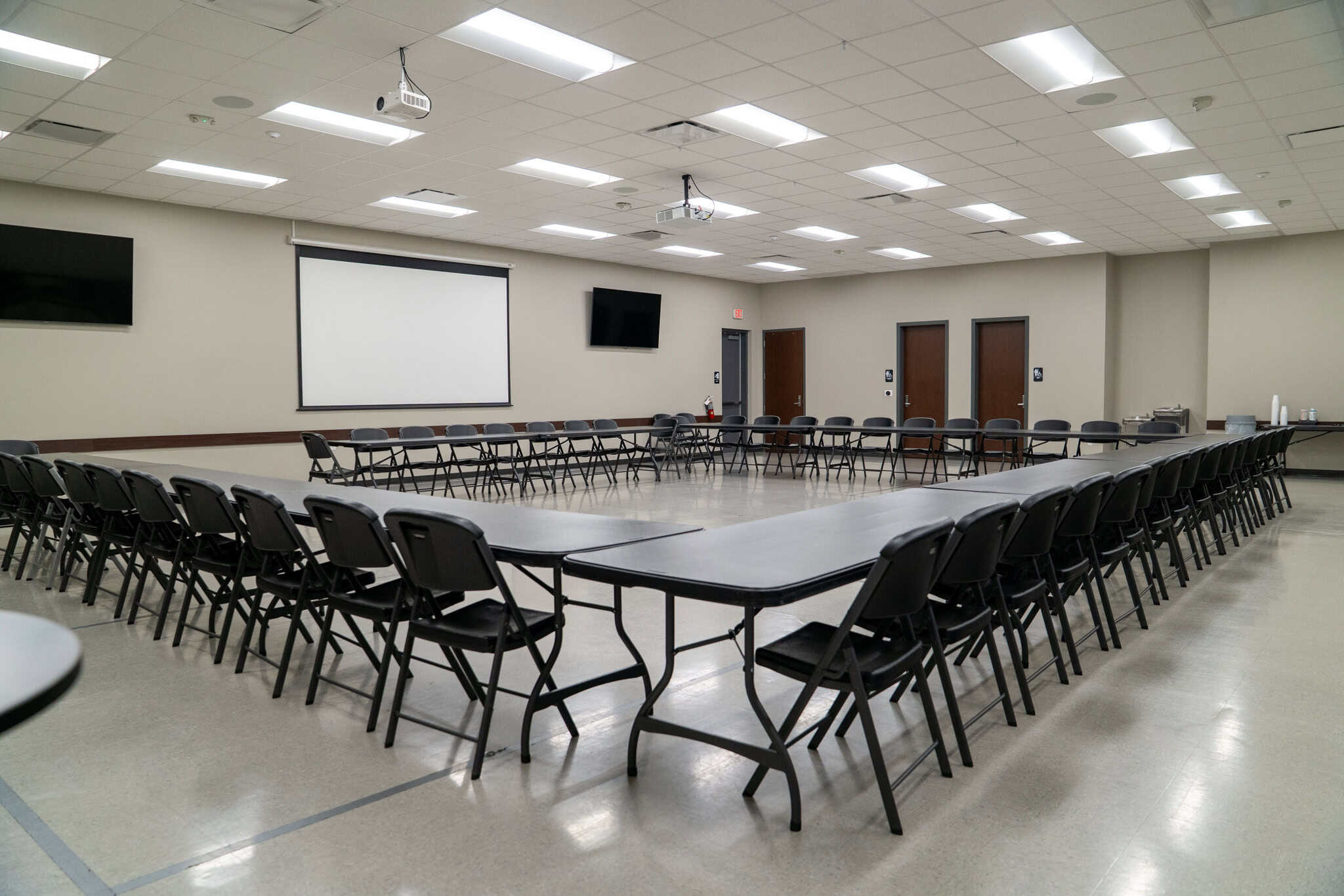 Spacious Gulf Coast conference room with tables and chairs arranged for meetings or events, equipped with multiple screens and modern lighting, ideal for corporate gatherings and seminars.