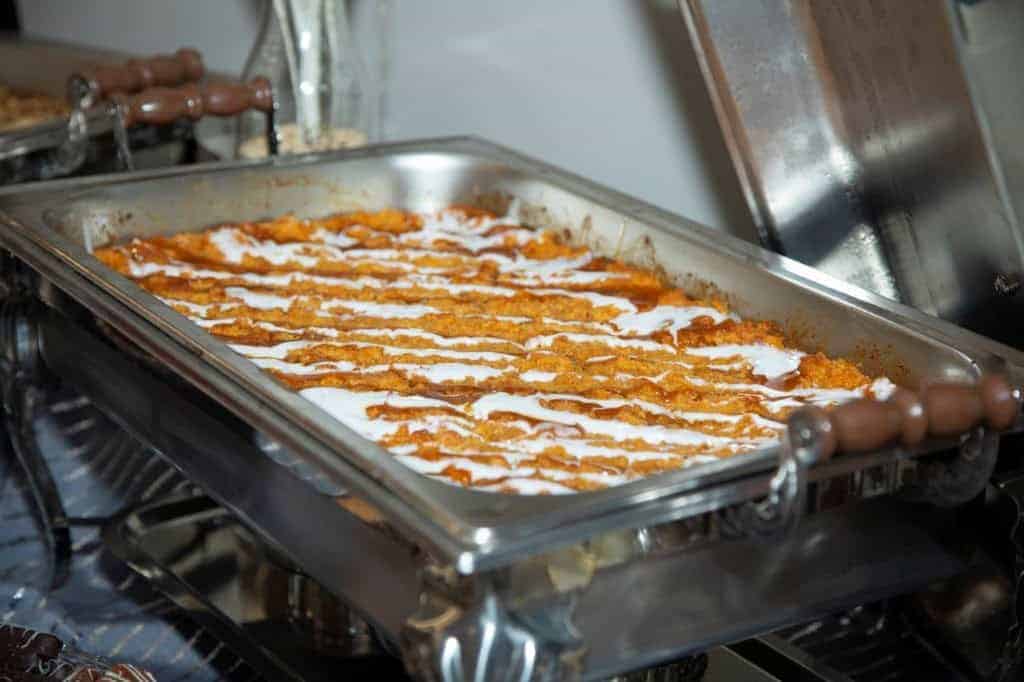 Creamy chicken and pasta casserole with a rich tomato sauce, topped with cheese, served in a stainless steel chafing dish at Gulf Coast gatherings. Perfect for a Southern-style event.